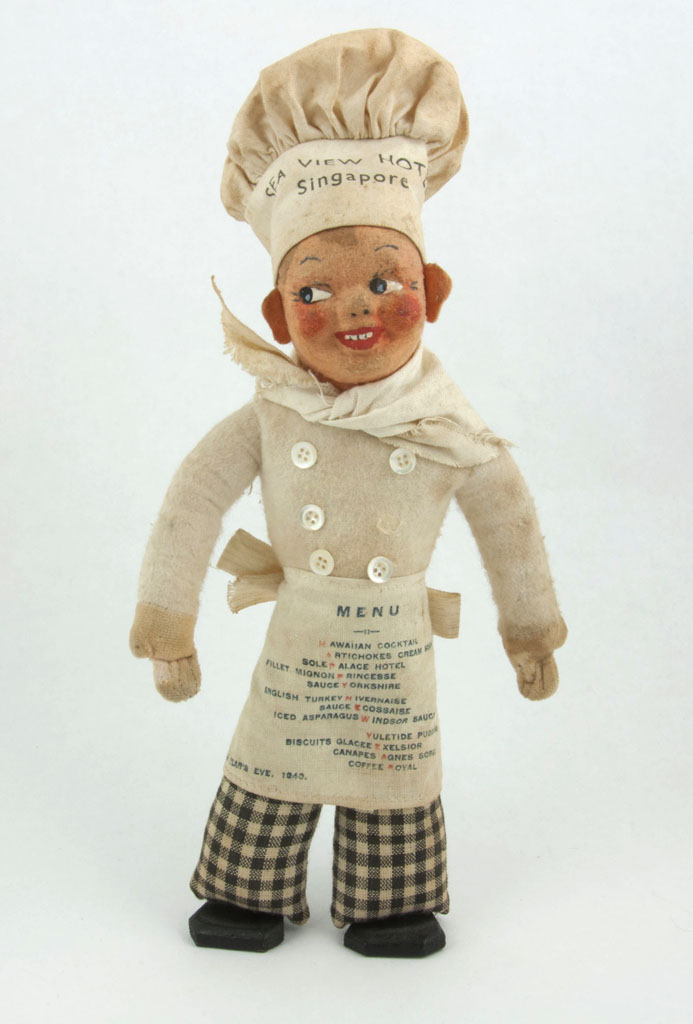 Cloth chef doll in a tall toque printed 'Sea View Hotel Singapore', with a menu printed on his apron